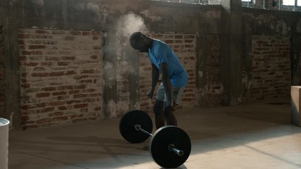 Sport man using chalk powder on hands and lifting weights at gym