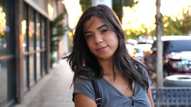 A beautiful young hispanic woman at sunset walking on the urban city street sidewalk while shopping at retail stores in slow motion.