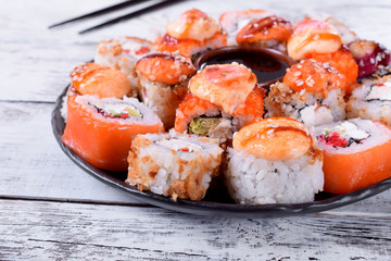 Sushi rolls assortment and soy sauce served on round plate on white wooden table
