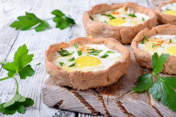 Baked rye tartlets with cheese and quail eggs on white wooden table
