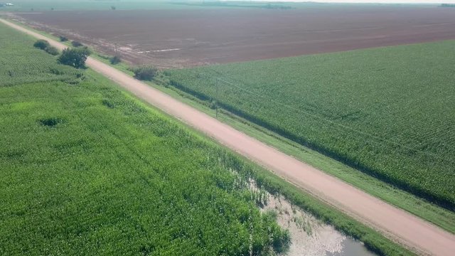 Drone aerial view a corn fields, a gravel road and a harvested field rural Nebraska, USA; there is standing water in the fields and ditches from recent rains