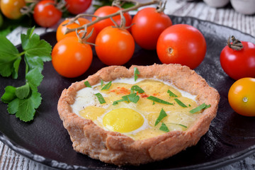 Baked rye tartlets with cheese and quail eggs on white wooden table