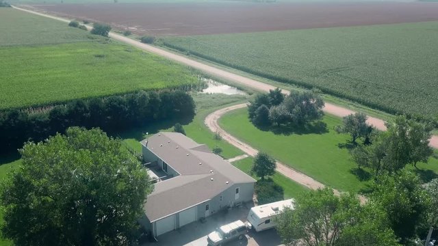 Drone aerial view of a sprawling home, farm yard, standing water, corn fields and a gravel road in rural Nebraska, USA