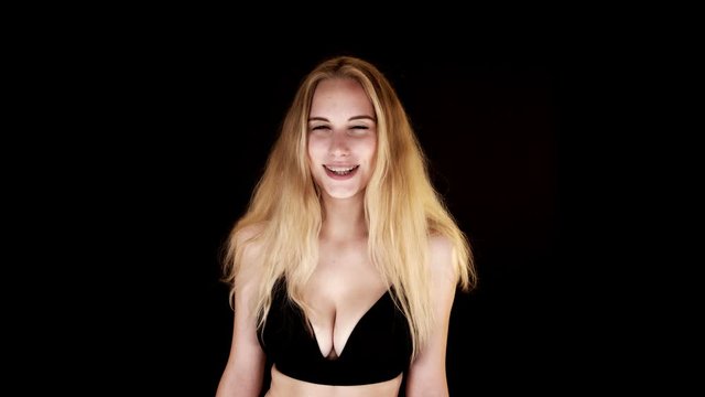 Close-up of a beautiful smilling blond woman in black underwear standing in front of a black background 