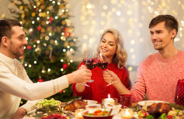 holidays and celebration concept - happy friends having christmas dinner at home, drinking red wine and clinking glasses