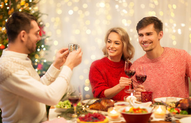 holidays and celebration concept - happy man photographing his friends at christmas dinner