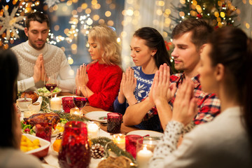 holidays and celebration concept - friends holding hands and praying while having christmas dinner...