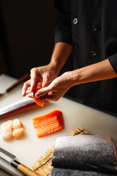 Closeup of chef hands preparing japanese food. Japanese chef making sushi at restaurant. Young chef serving traditional japanese sushi served on a cuting board in lighting studio