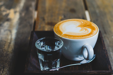 close up modern hot black coffee the cappuccino on wood background with coffee bubble foam pattern and texture in white cup looking and feel so delicious on glasses table in coffee shop.