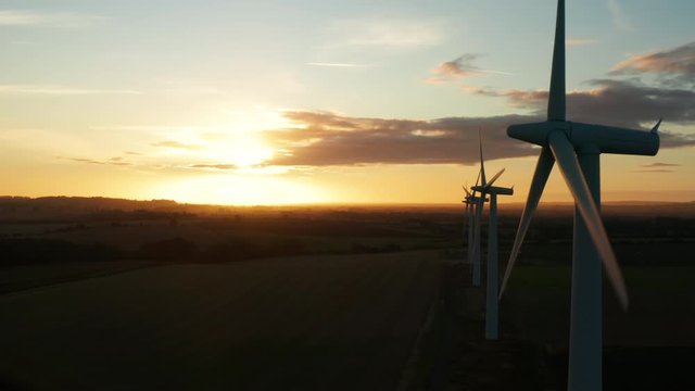 Aerial view across large wind turbines at sunrise on a clear day slowly orbiting around them in the English countryside