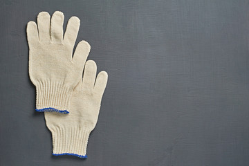 Pair of protective white textile gloves for hard work lies on dark scratched concrete table in workshop. Space for text. Top view