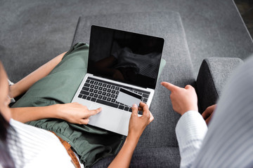 cropped view of multicultural friends holding credit card and using laptop in apartment