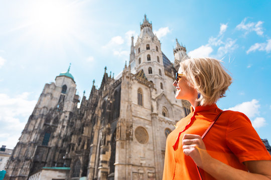 A young woman in a bright orange dress stands on the background of St. Stephen's Cathedral in Vienna, Austria