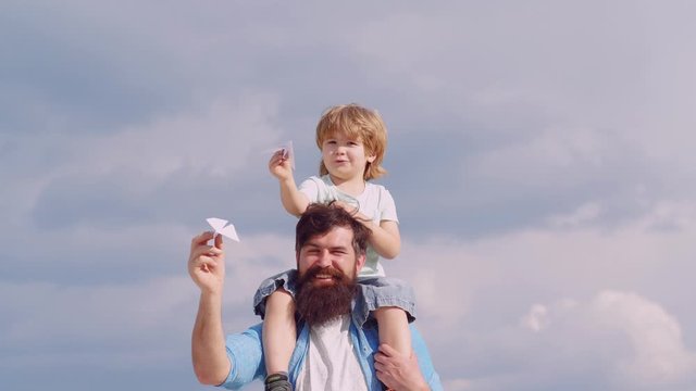 Happy father and son on meadow in summer. Child pilot aviator with airplane dreams of traveling. Concept of Father's day. Happy father giving son piggyback ride on his shoulders on sky background.