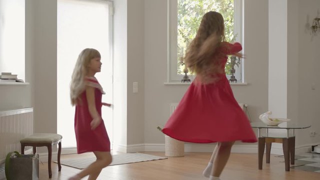 Blond caucasian mother and daughter hacing fun at weekends. Beautiful woman and cheerful girl in the same red dresses dancing. Happy family spending day together.