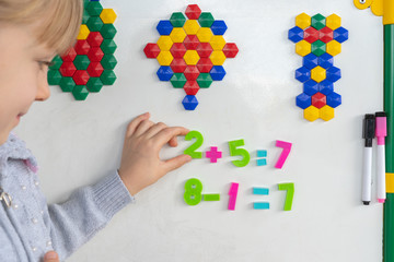 Little preschooler girl on magnetic interactive white borad is studying addition and subtraction in math lesson. Education School Preschool concept.