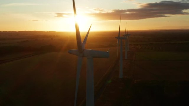 Aerial view across large wind turbines at sunrise on a clear day slowly orbiting around them in the English countryside