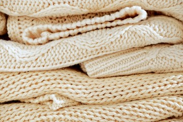 Fototapeta na wymiar Close-up of knitted clothes in warm beige shades with a different pattern of the fall / winter season texture, background. With selective focus, copy space for text.