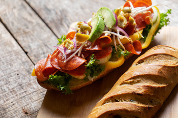 Salami sub sandwich in rustic baguette with olives and sprouts