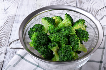 Blanched broccoli cabbage florets in a sieve on white wooden table