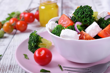 Light salad with broccoli, cherry tomatoes and feta cheese in a white ceramic bowl
