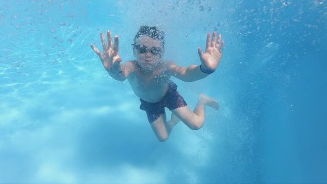 Boy with his thumbs up swimming underwater in summer pool. Happy holidays concept