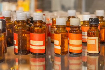 Shelf with brown pharmacy bottles with blank labels reflected on the glass some capped, some open