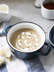 Aubergine soup with cream and thyme in small blue pot on grey background.
