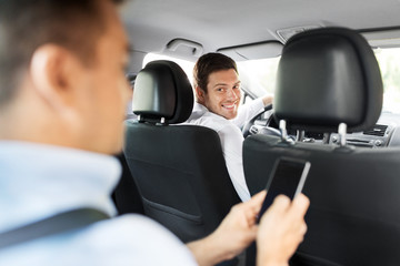 transportation, vehicle and people concept - male car driver looking at passenger with smartphone...