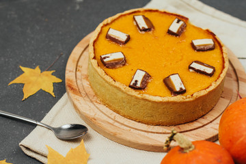  pumpkin pie on a wooden board, yellow autumn leaves and small pumpkins on a dark gray background. halloween treat.