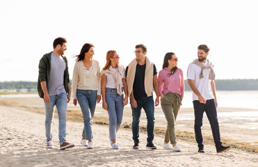 Obraz premium friendship, leisure and people concept - group of happy friends walking along beach in summer