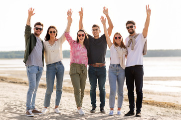 Obraz premium friendship, leisure and people concept - group of happy friends waving hands on beach in summer
