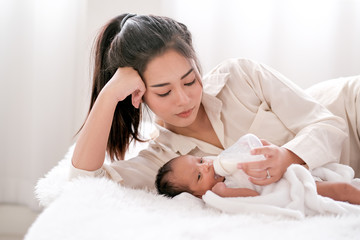 Beautiful Asian mother lie on white bed and give milk to her newborn baby.