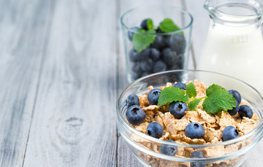 Multigrain cereal bowl with fresh blueberries and mint leaves and jug of milk, healthy breakfast concept