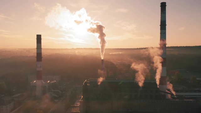 Factory chimneys producing smoke at sunrise, aerial view. Concept of air pollution, environment and ecology crisis, climate change, global warming.