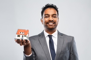 real estate business and people concept - indian man realtor with house model over grey background