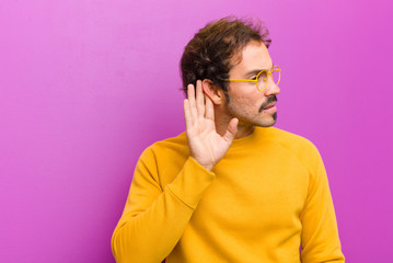 young handsome man looking serious and curious, listening, trying to hear a secret conversation or...