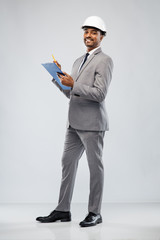 architecture, construction business and people concept - smiling indian male architect in helmet with clipboard over grey background