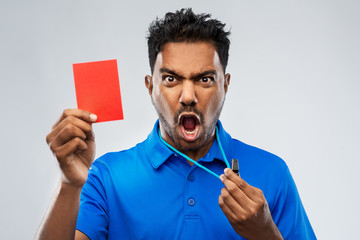 sport, caution, game and football concept - angry indian male referee with whistle and showing red...