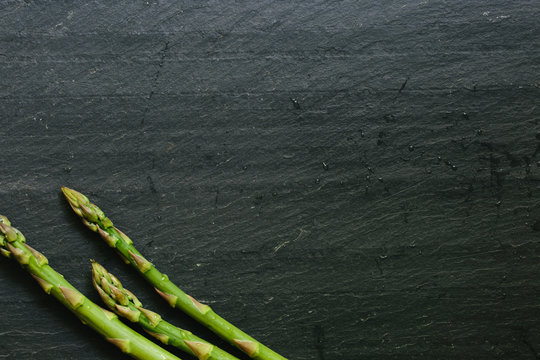 Three fresh picked asparagus spears on black slate countertop