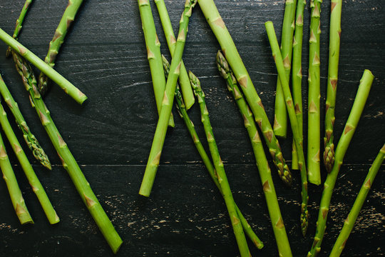 Fresh cut asparagus spears lay on a black painted rustic wooden table
