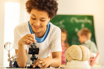 Pleased brunette kid looking through the microscope