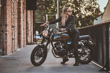 Female biker in full leather suit is posing for photographer while sitting on her brand new motorbike.