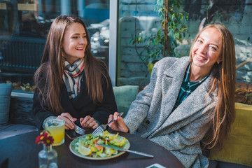 two girlfriends talking while eating in outdoors cafe autumn time
