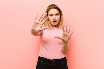 young pretty blonde woman feeling terrified, backing off and screaming in horror and panic,...