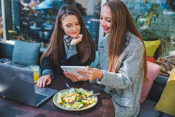 two young adult women have meeting in outdoors cafe working on laptop