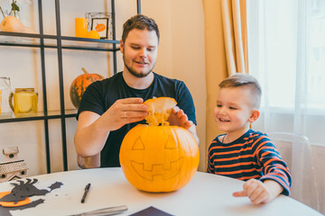 young father with toddler son making jack pumpkin head for halloween holiday