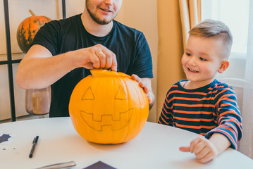 young father with toddler son making jack pumpkin head for halloween holiday