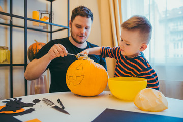 young father with toddler son making jack pumpkin head for halloween holiday