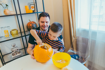young father with toddler son making jack pumpkin head for halloween holiday